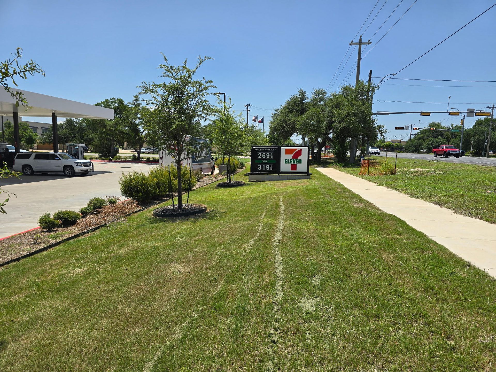 7-Eleven gas station with prices displayed, a green grassy area, and a sidewalk.