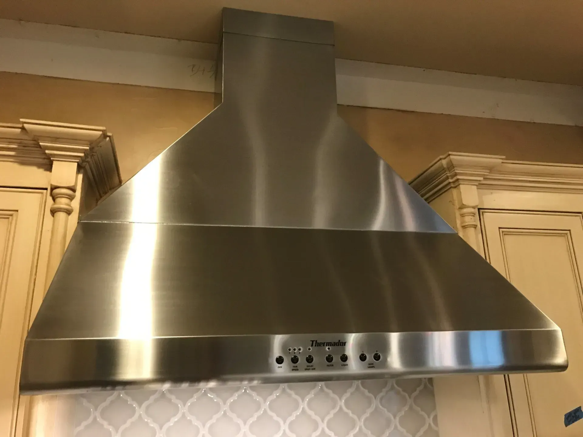 A stainless steel hood is hanging from the ceiling in a kitchen.