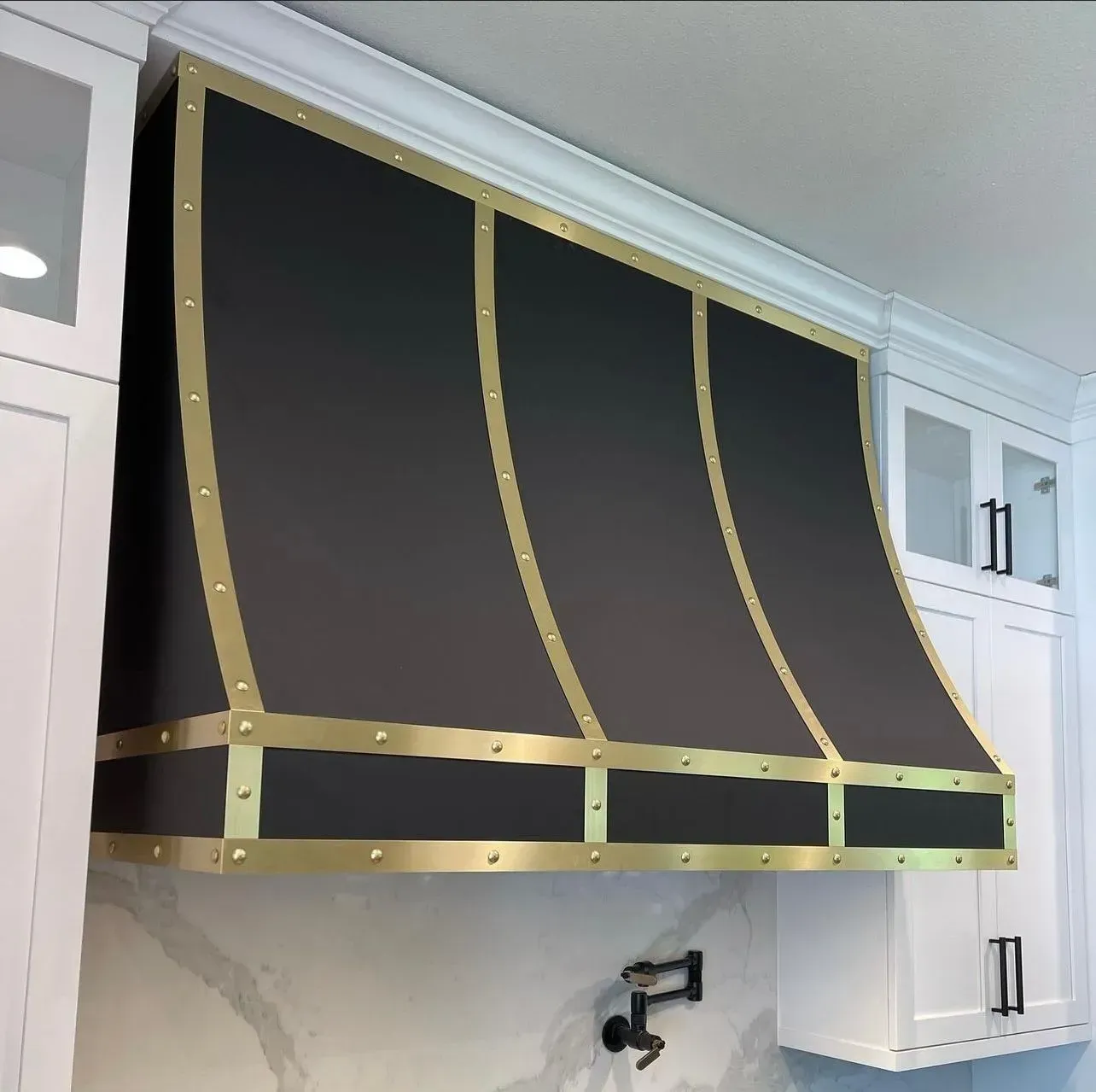 A black and gold hood in a kitchen with white cabinets