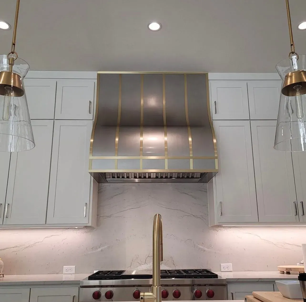 A kitchen with white cabinets , a stove , a sink and a hood.