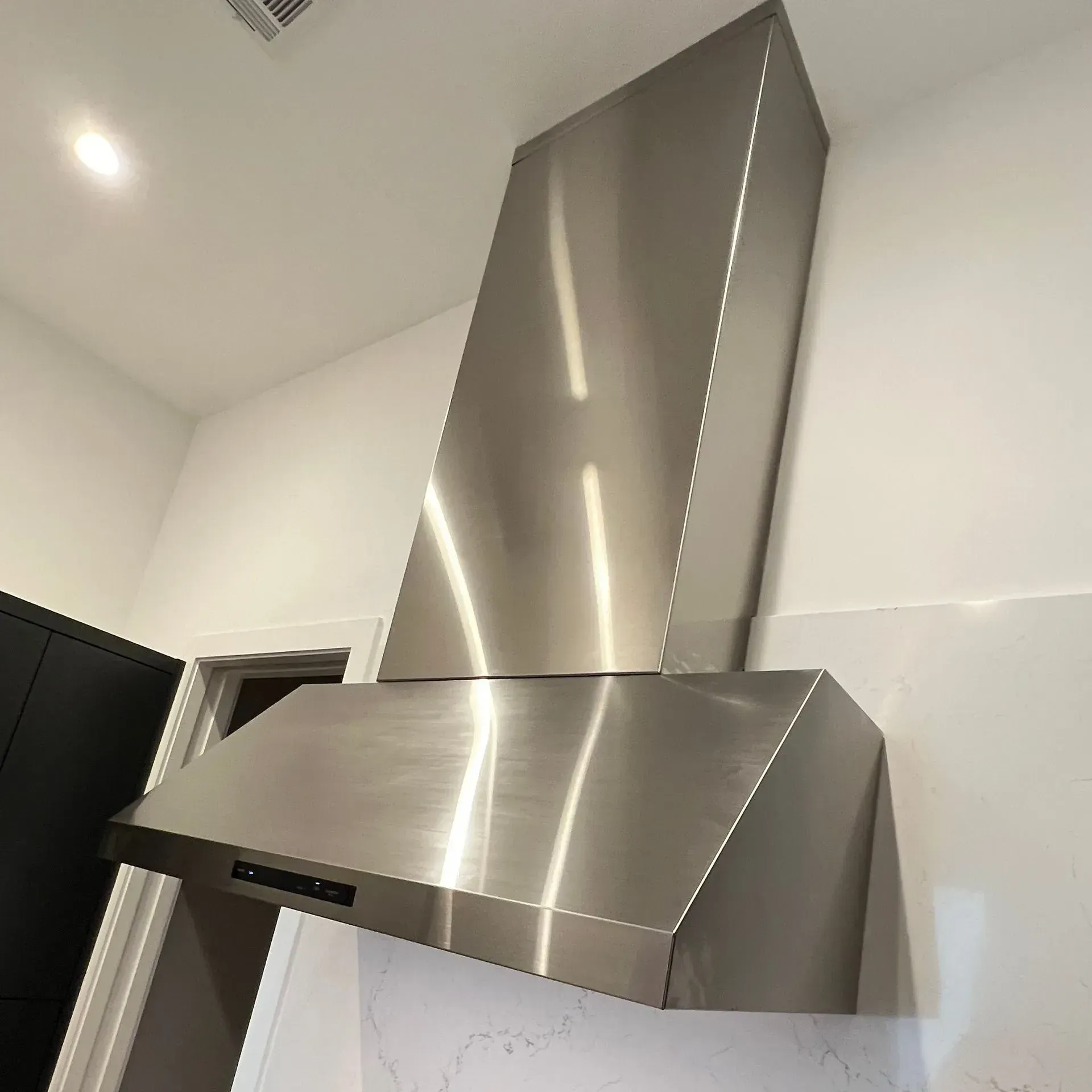 A stainless steel hood is hanging from the ceiling in a kitchen.