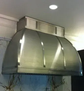 A stainless steel hood is hanging from the ceiling in a kitchen.