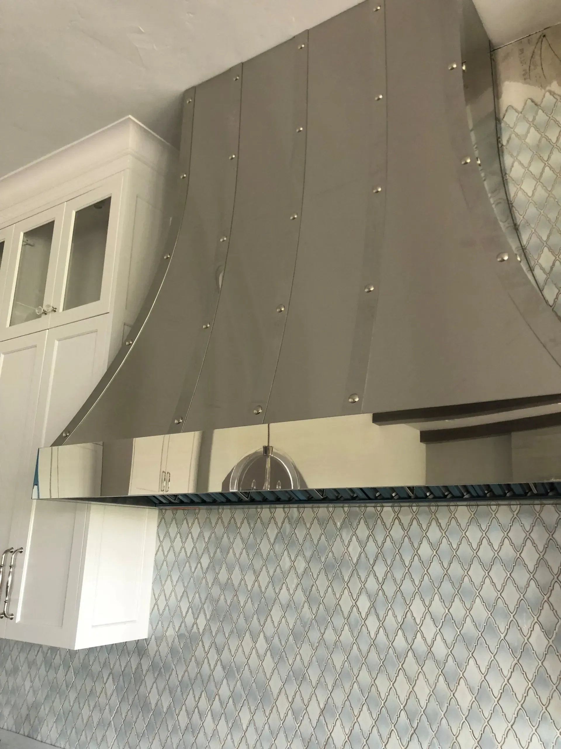 A stainless steel hood is hanging from the ceiling in a kitchen.