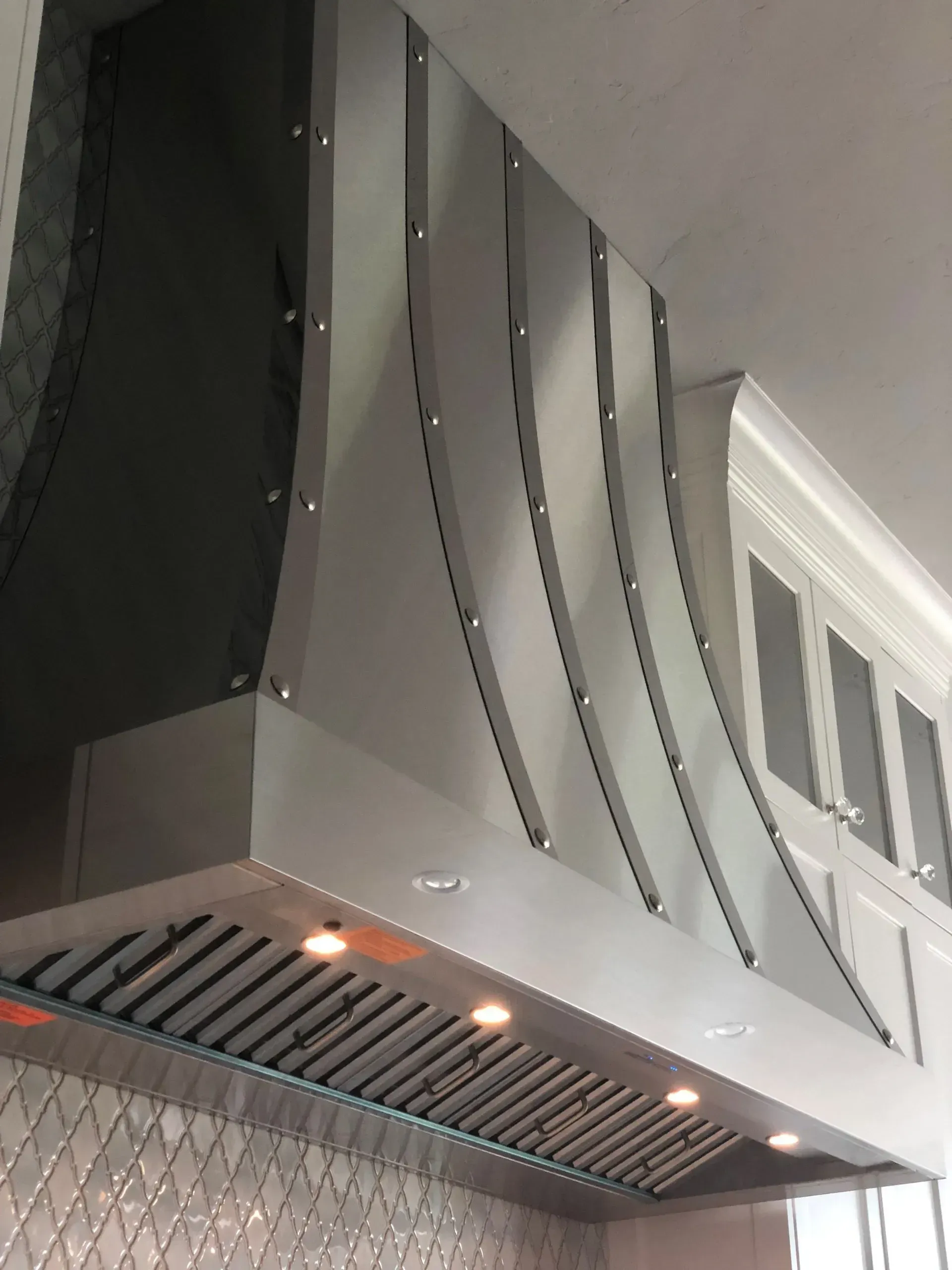 A stainless steel hood is hanging from the ceiling in a kitchen