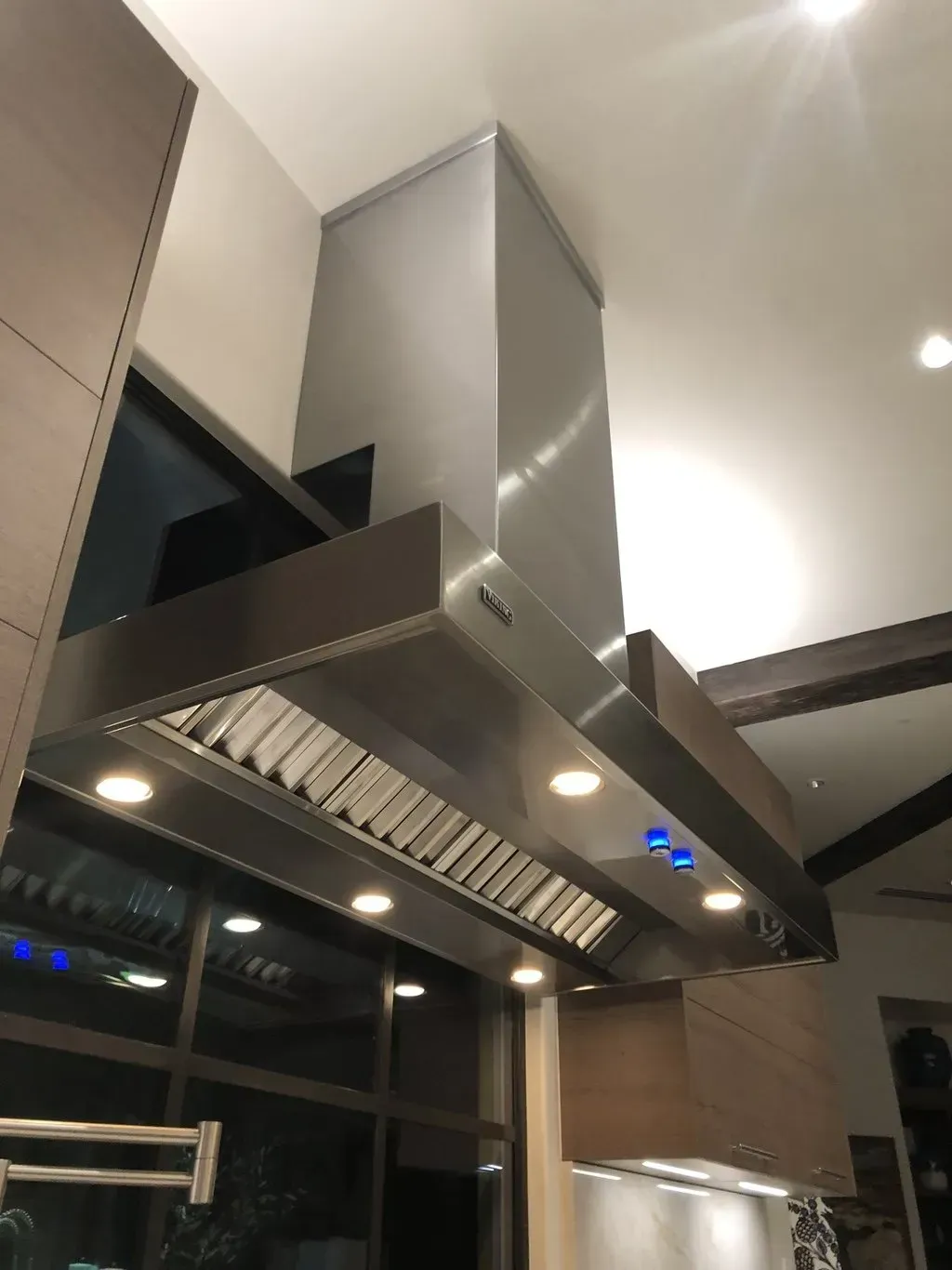 A stainless steel hood is hanging from the ceiling of a kitchen.