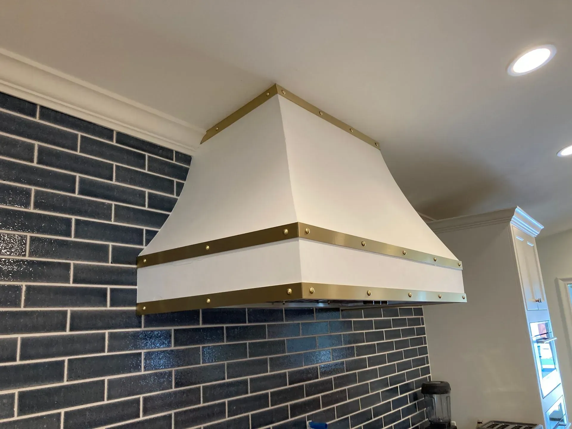 A white and gold hood is hanging from the ceiling in a kitchen.