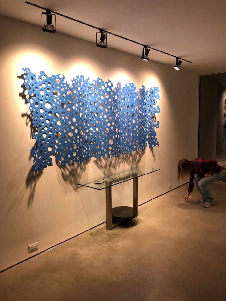 A woman is bending over in front of a wall with a blue sculpture on it