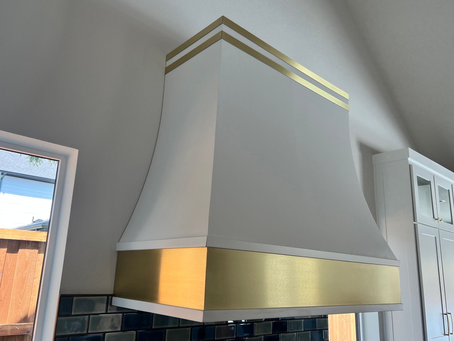 A white and gold hood is hanging from the ceiling in a kitchen.