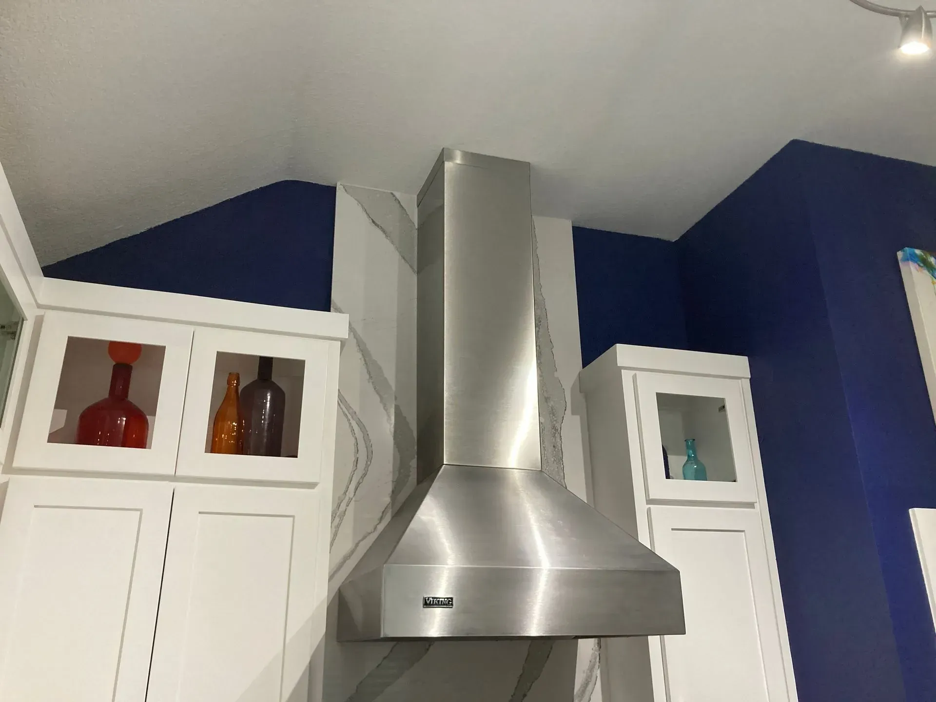 A stainless steel hood is hanging from the ceiling in a kitchen.