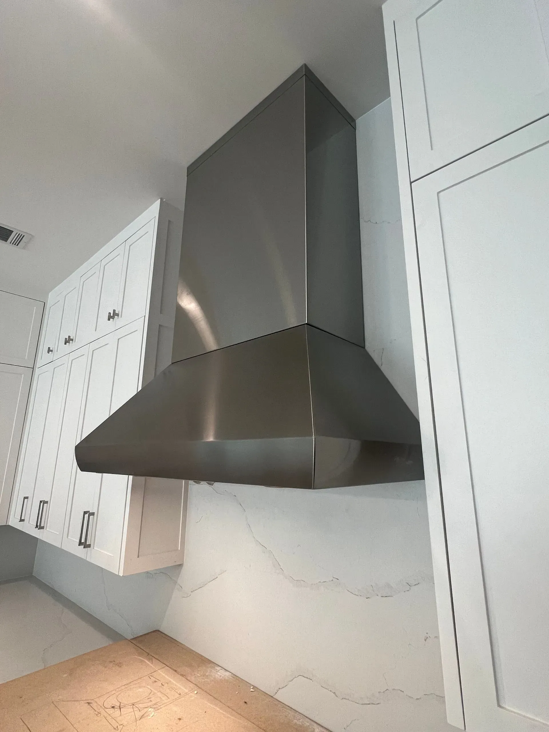 A kitchen with white cabinets and a stainless steel hood