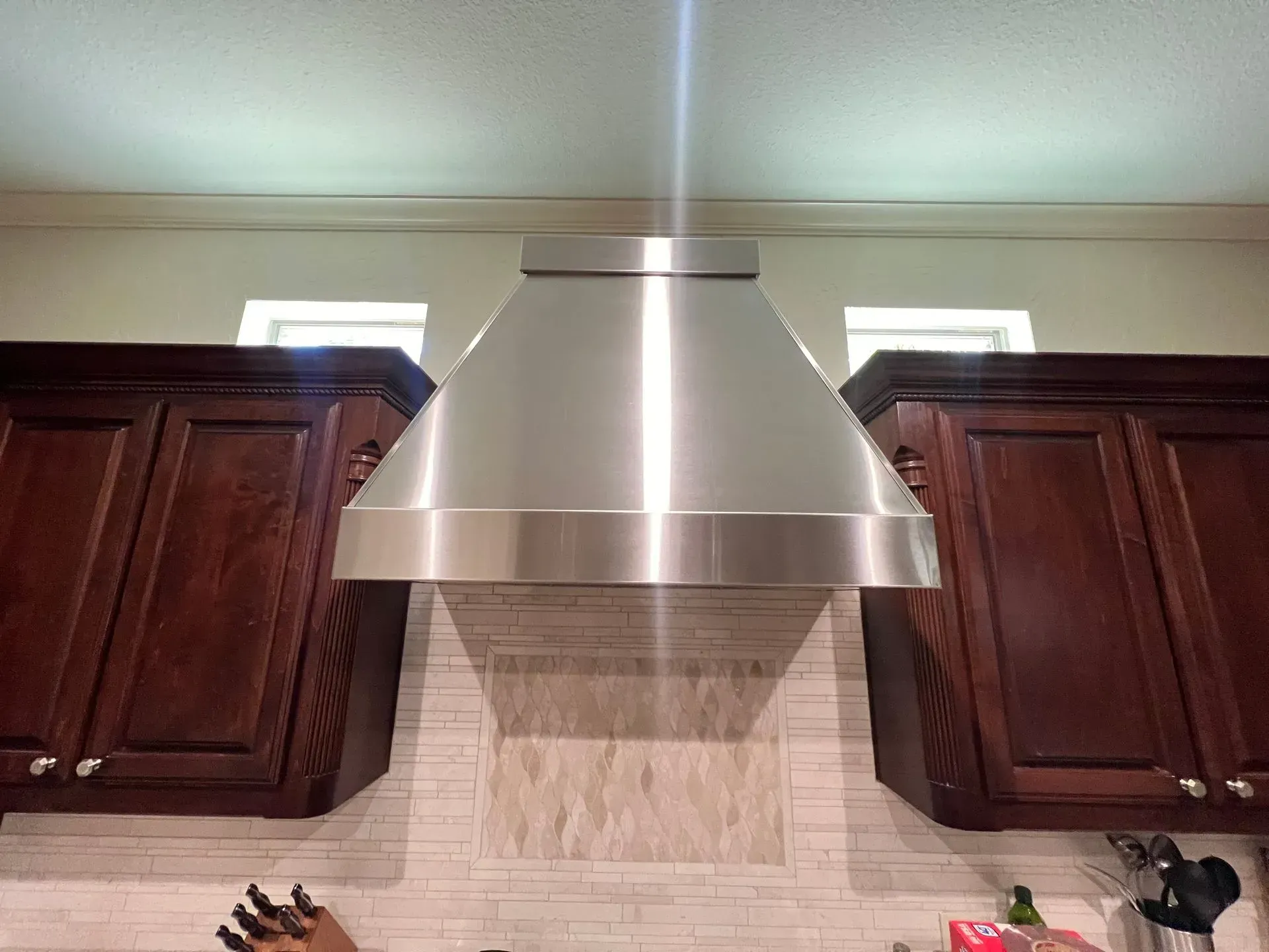 A stainless steel hood is hanging from the ceiling in a kitchen.