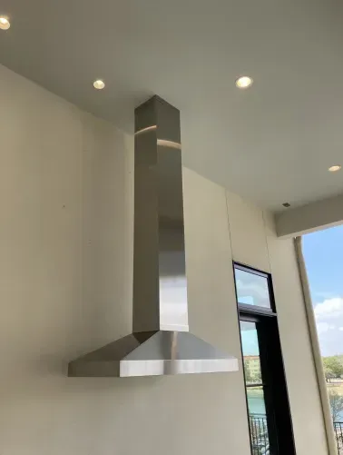 A stainless steel hood is hanging from the ceiling in a kitchen.