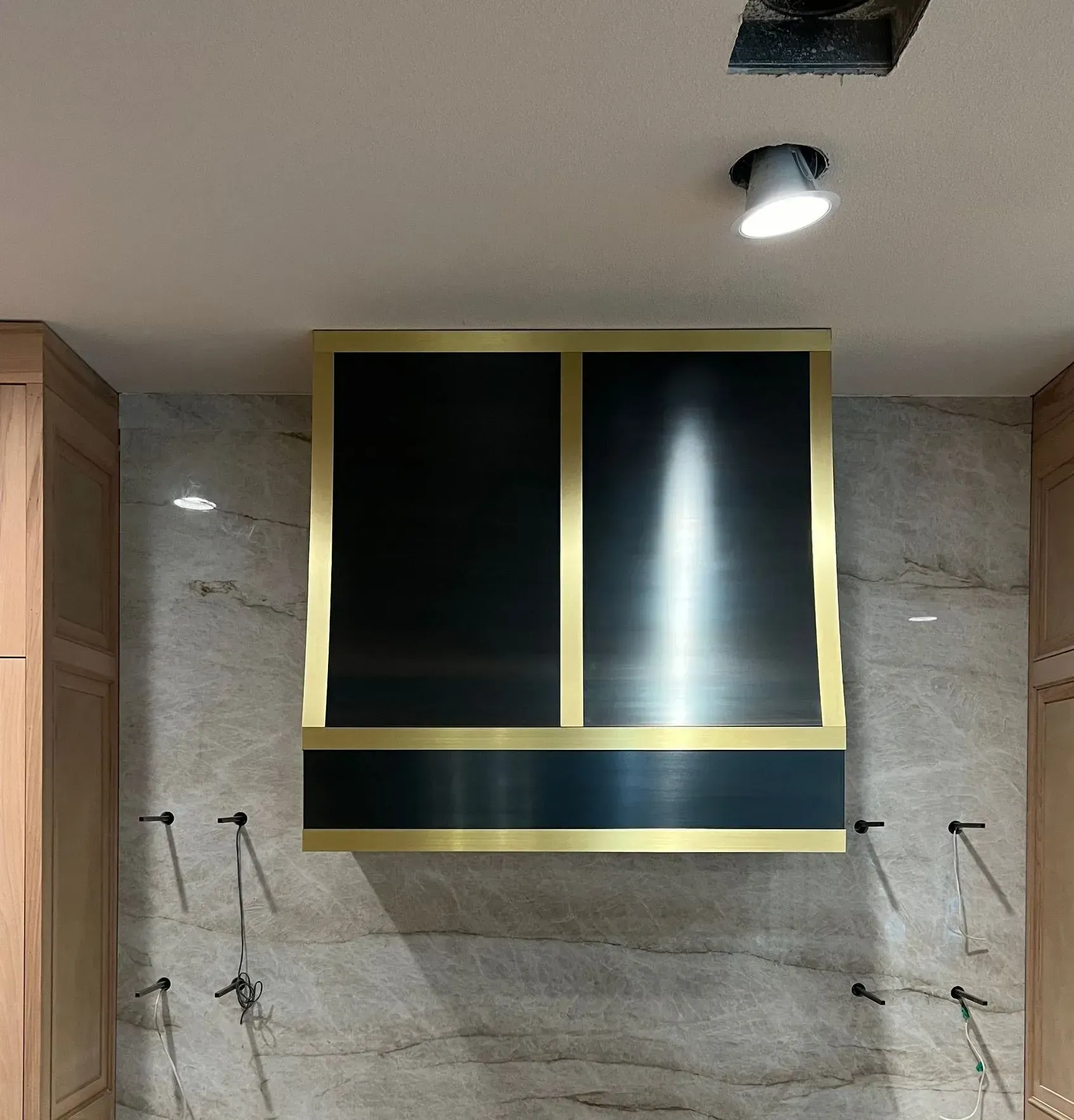 A black and gold hood is hanging from the ceiling in a kitchen