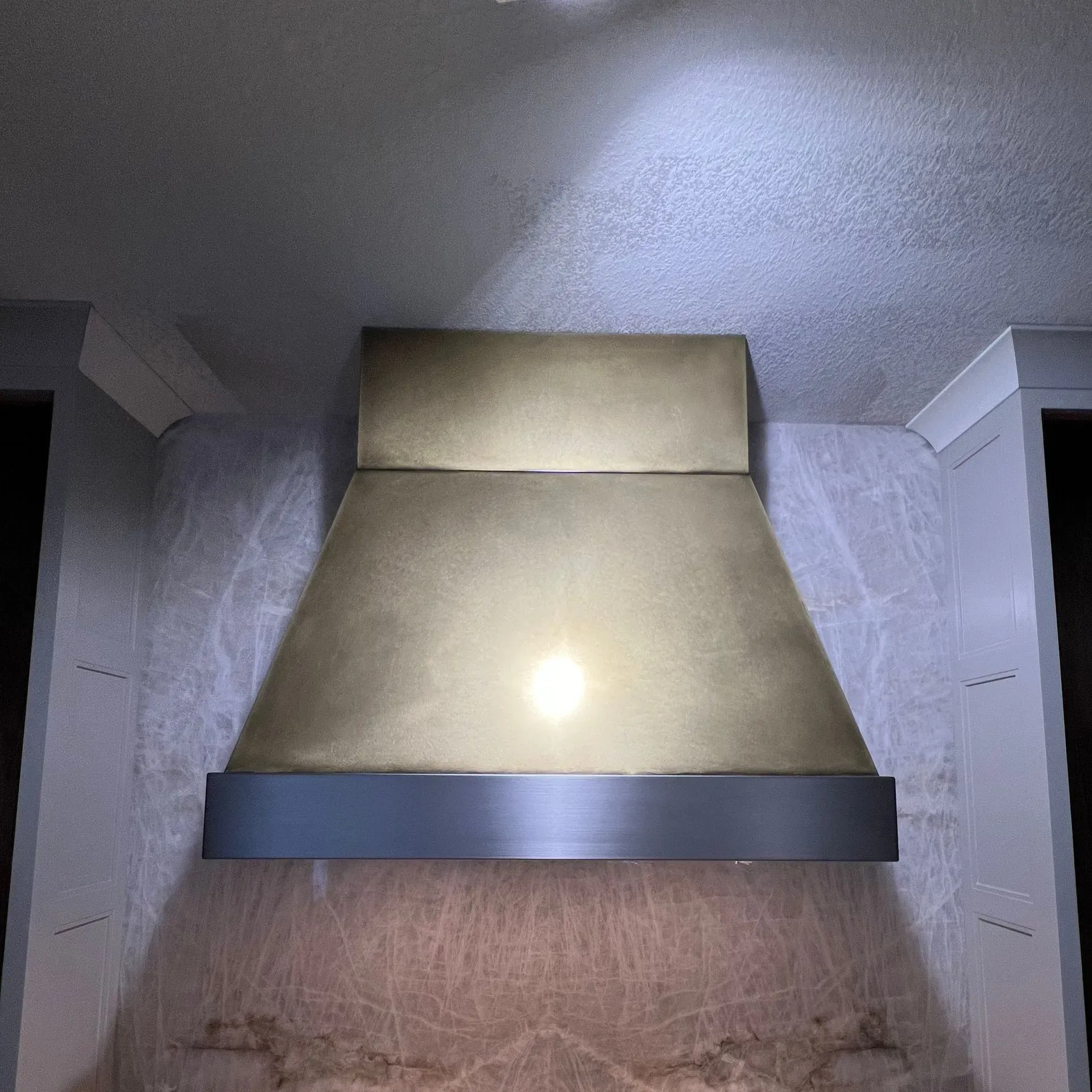 A brass hood is hanging from the ceiling in a kitchen