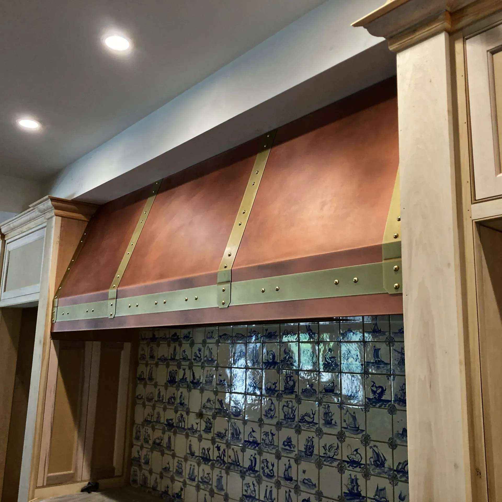 A kitchen with a copper hood and blue and white tiles