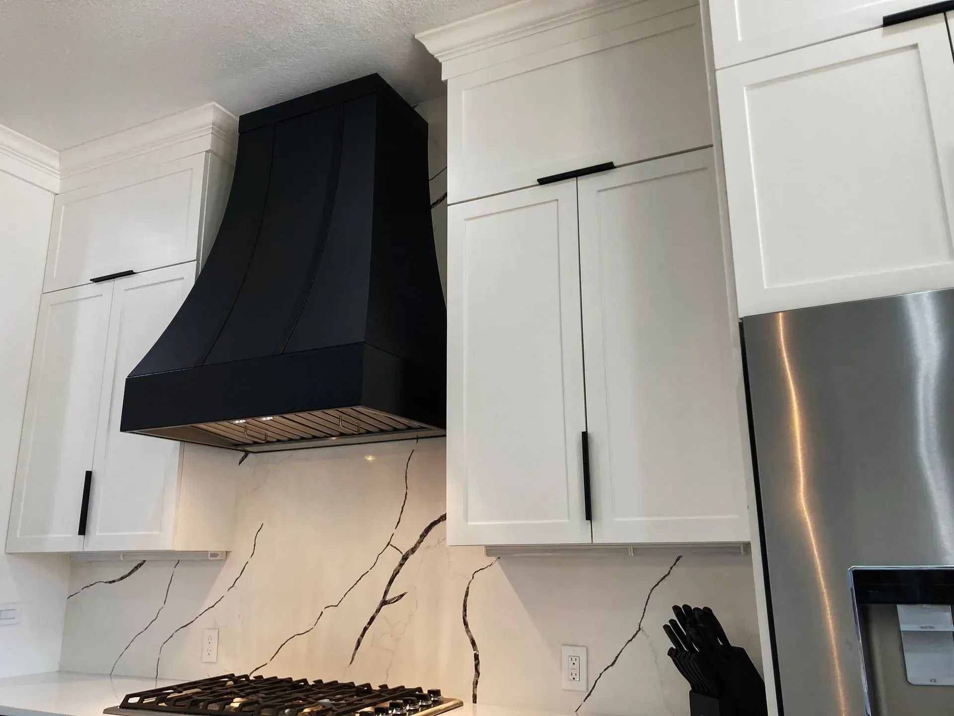 A kitchen with white cabinets and a black hood