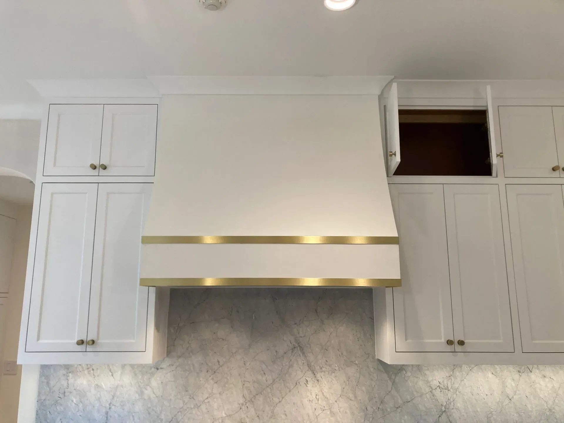 A kitchen with white cabinets and a brass hood