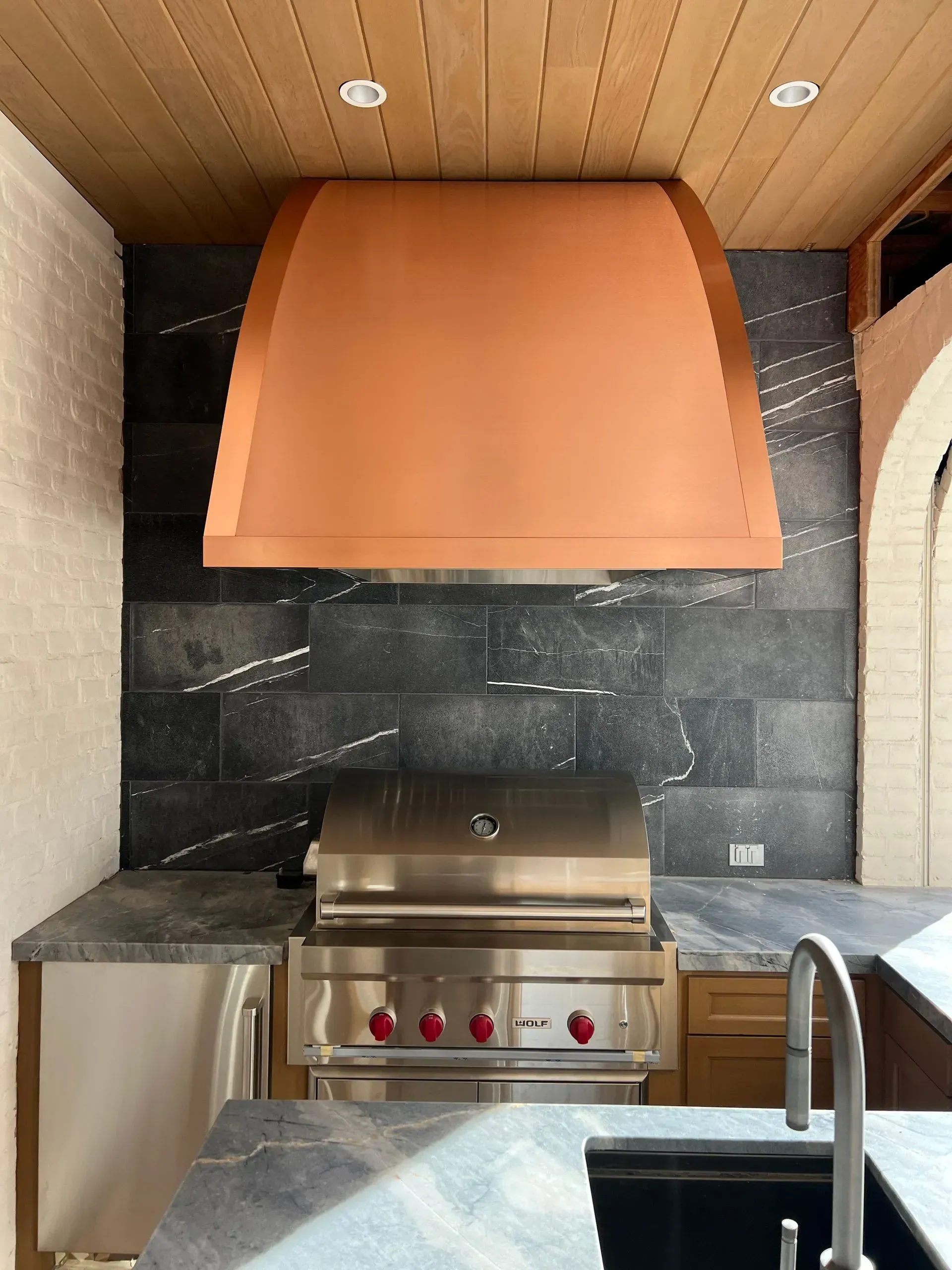 A kitchen with a copper hood over a grill and a sink