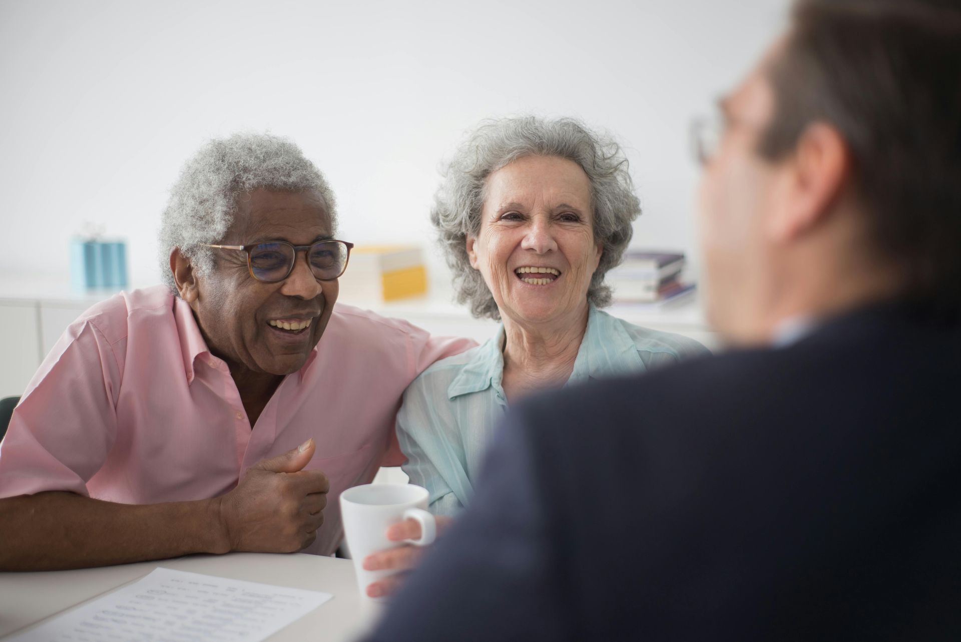 Couple smiling, meeting with person in suit at a table. Bright room.