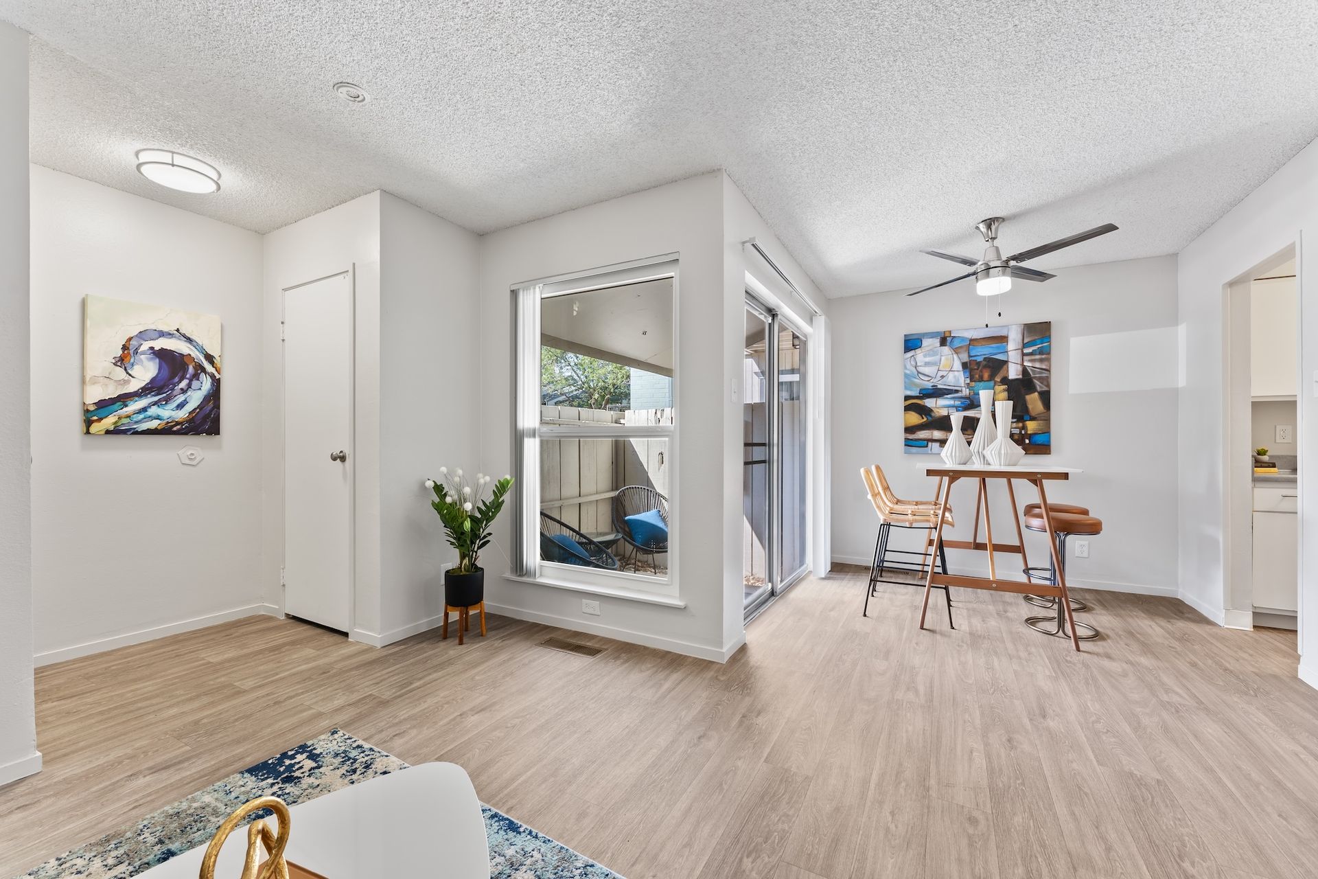 Bright living room with hardwood floors, art, and a small dining table near sliding glass doors.