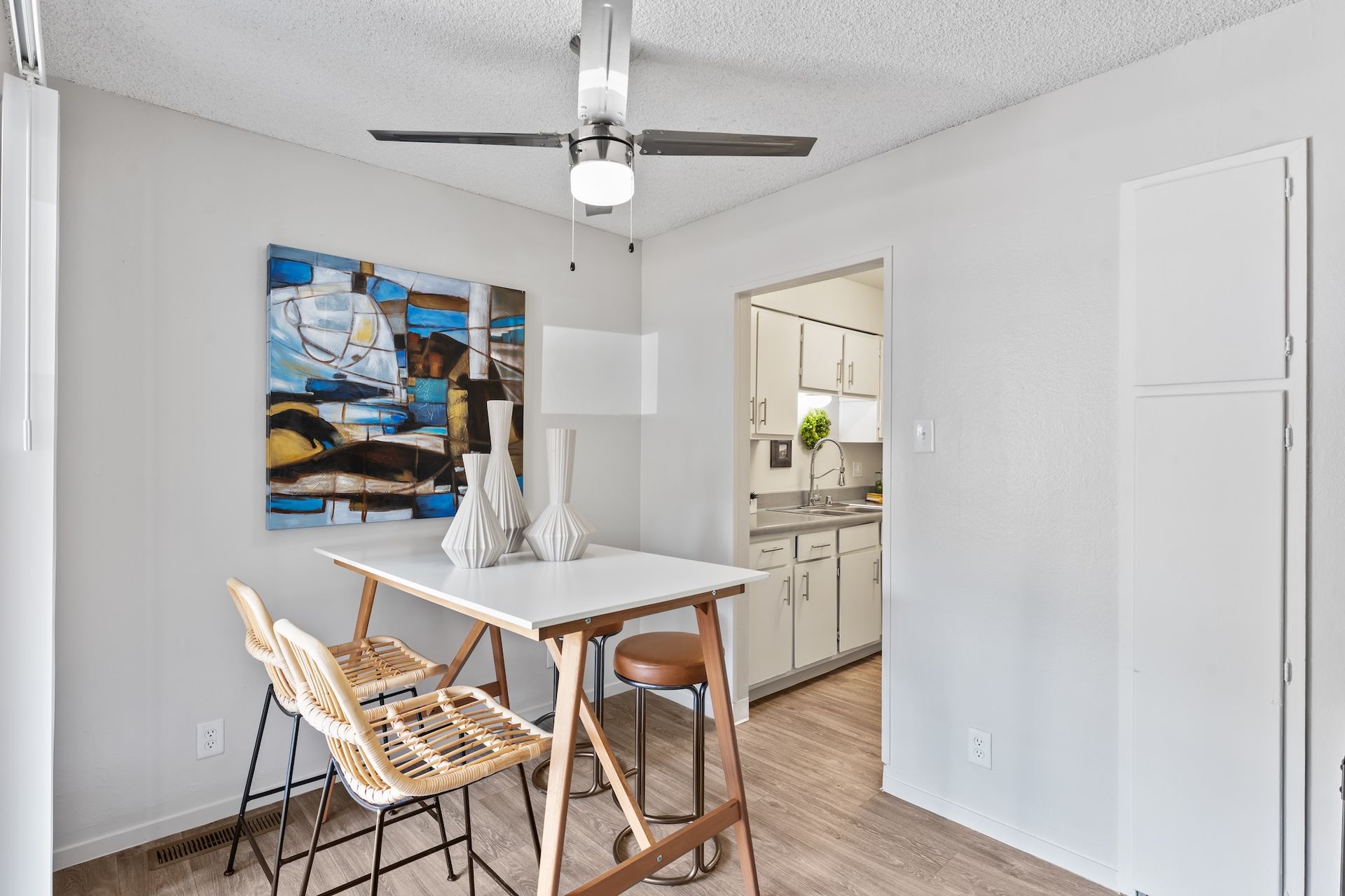 Dining area with white table, chairs, and artwork; opening to a kitchen.
