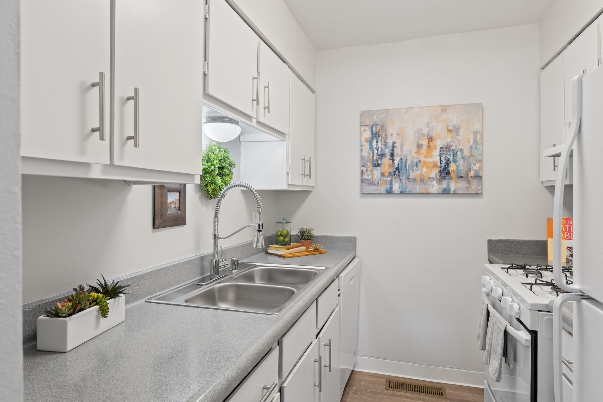 White kitchen with cabinets, sink, appliances. Artwork on wall.