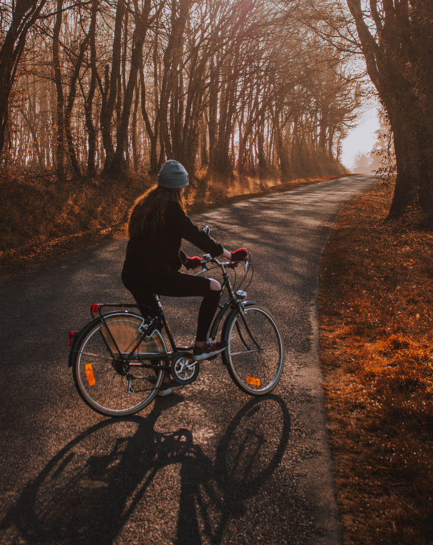 A woman is riding a bike down a road in the woods.