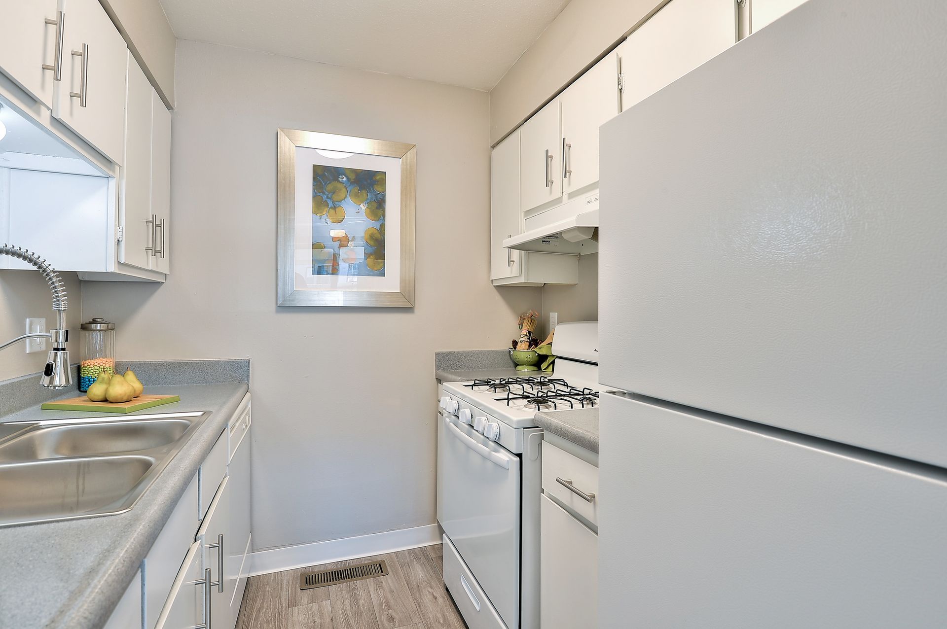 A kitchen with white cabinets , a refrigerator , a stove , a sink and a picture on the wall The Park at Idlewild. 