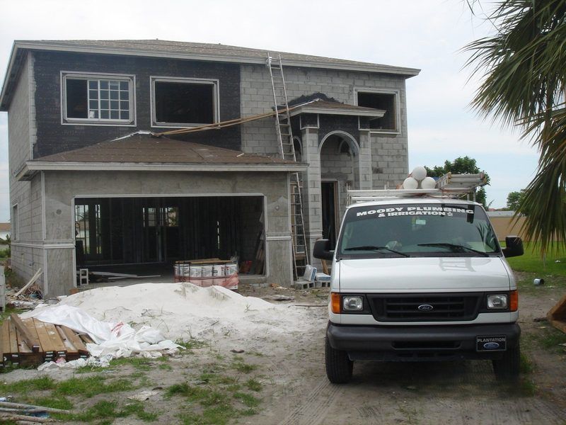A two-story house under construction with stucco walls and an open garage, parked next to a white service van.