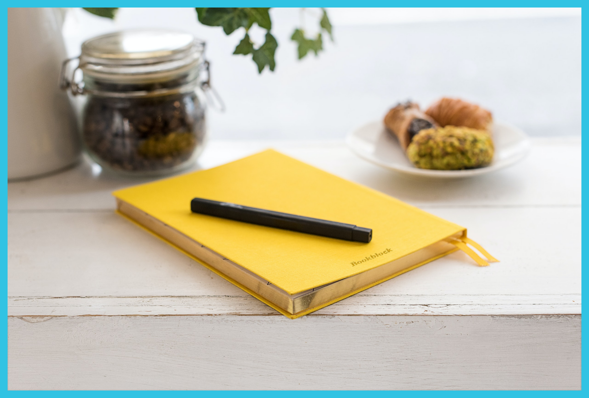 A yellow notebook with a pen and a jar of coffee on a table.