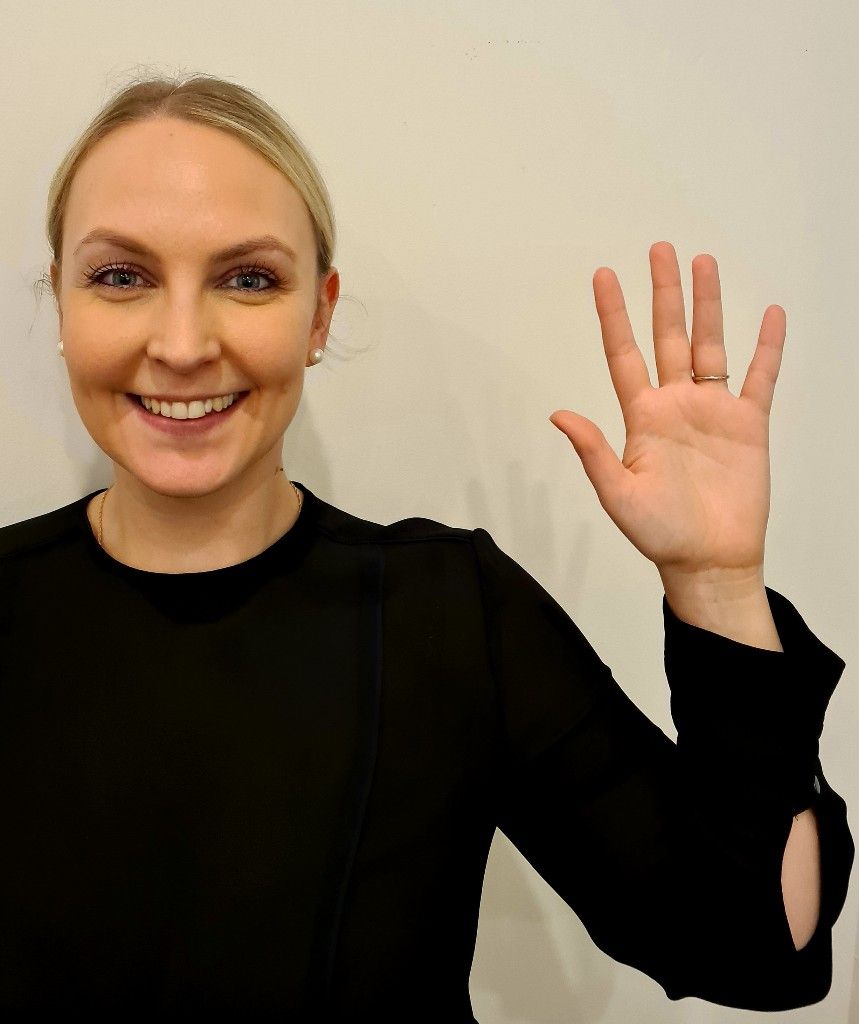 A woman in a black shirt is smiling and waving her hand