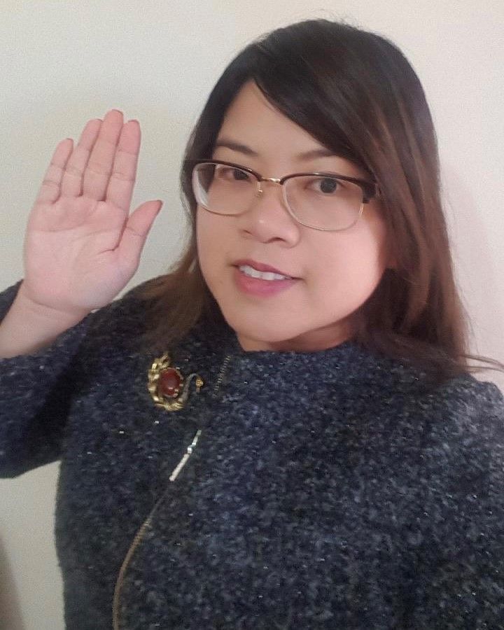 A woman wearing glasses and a brooch is waving her hand