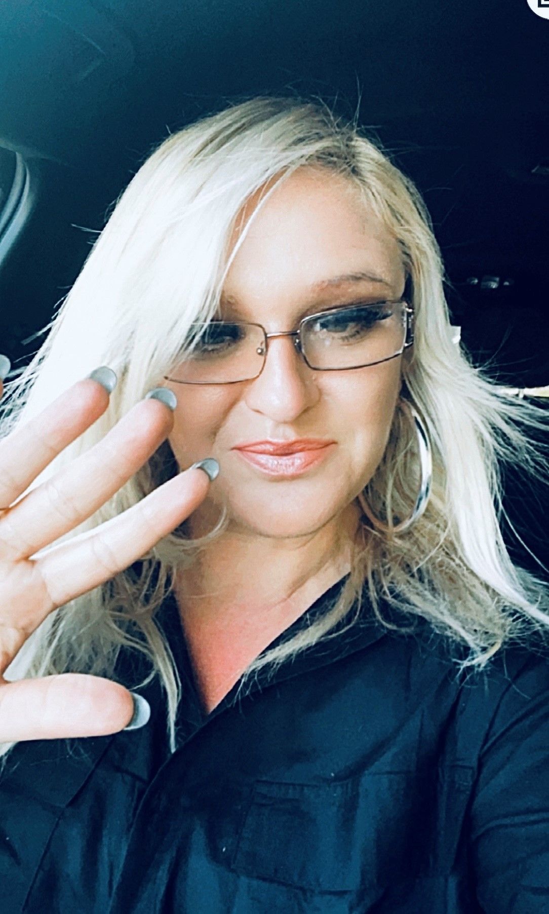 A woman wearing glasses and a black shirt is taking a selfie in a car.