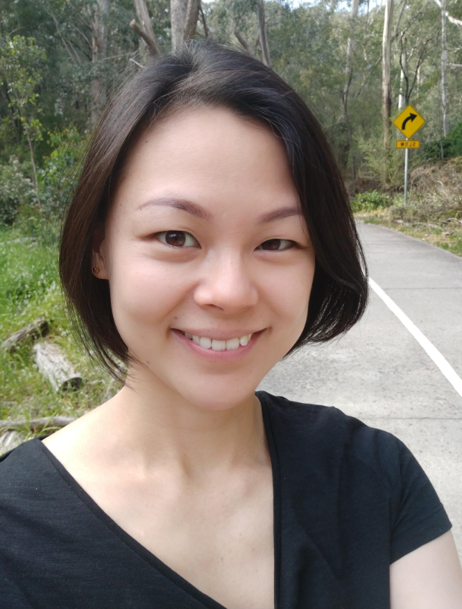 A woman in a black shirt is smiling in front of a road.