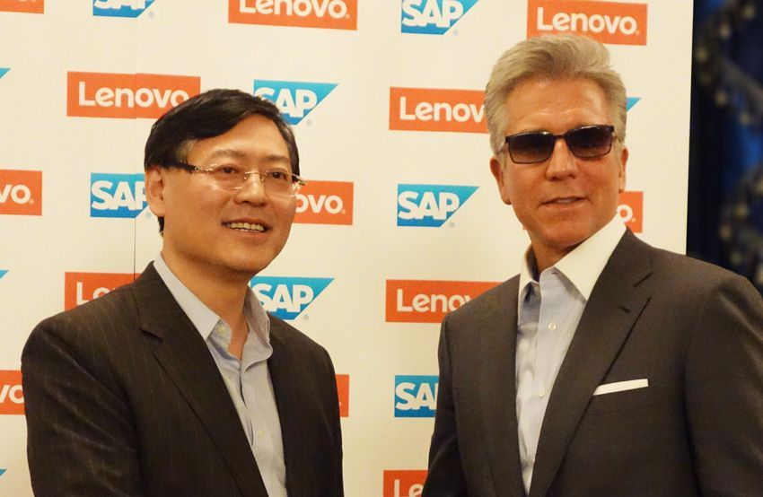 Two men are posing for a picture in front of a wall that says lenovo