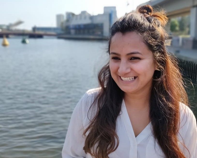 A woman in a white shirt is smiling in front of a body of water.