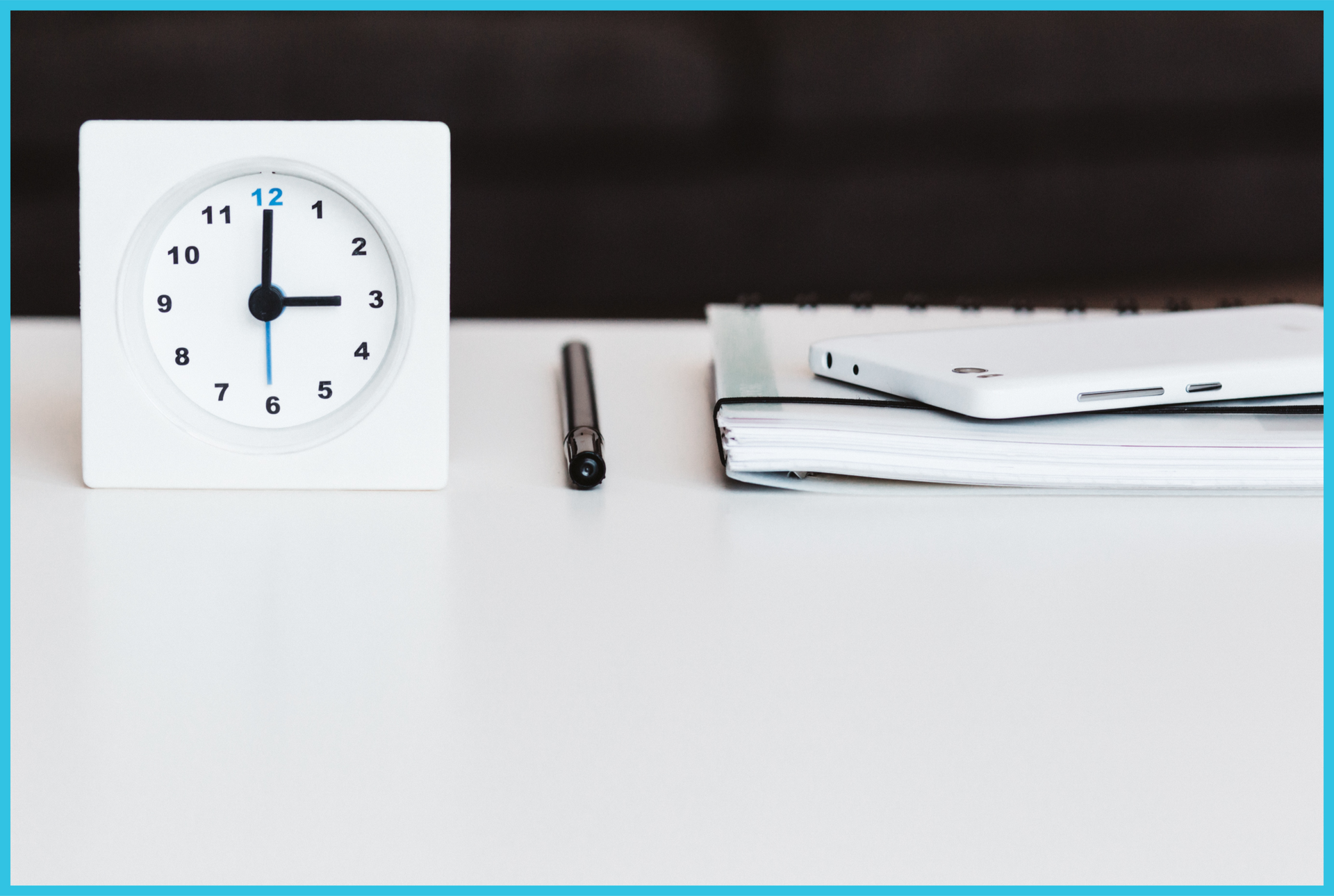 A white clock is sitting on a table next to a pen and a notebook.