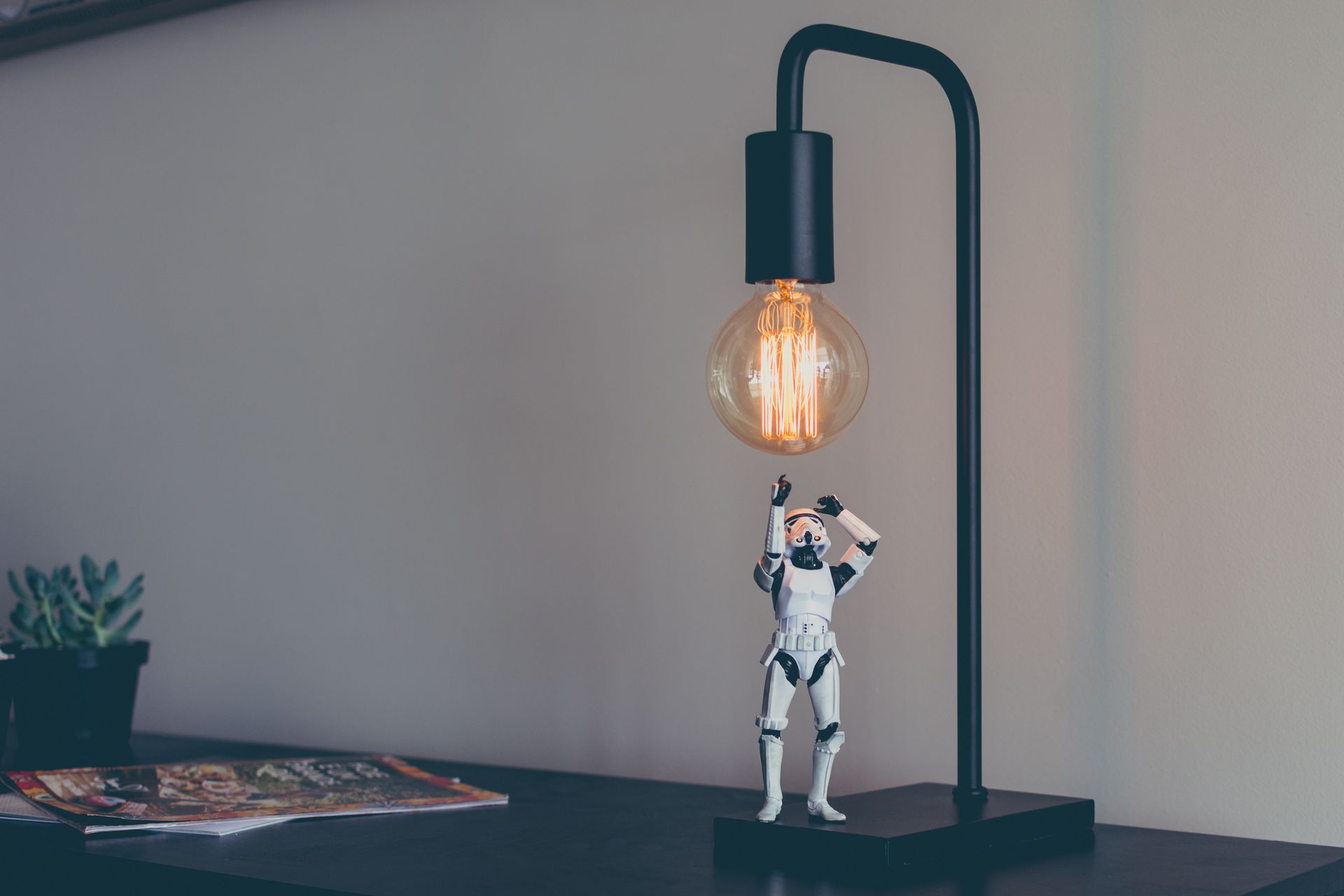 A storm trooper figurine is standing next to a lamp on a table.