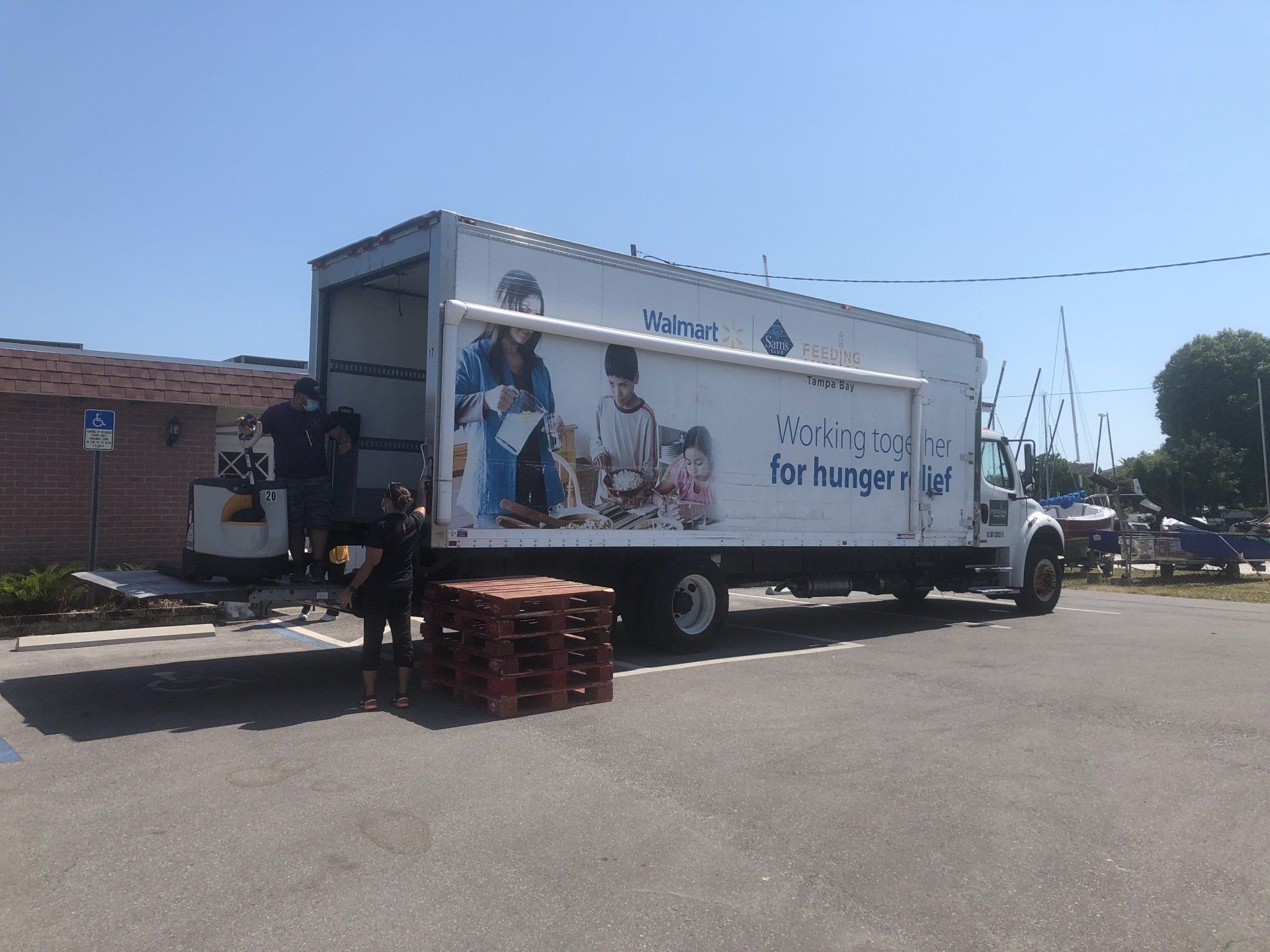People unloading a food truck with pallets. Sunny day.