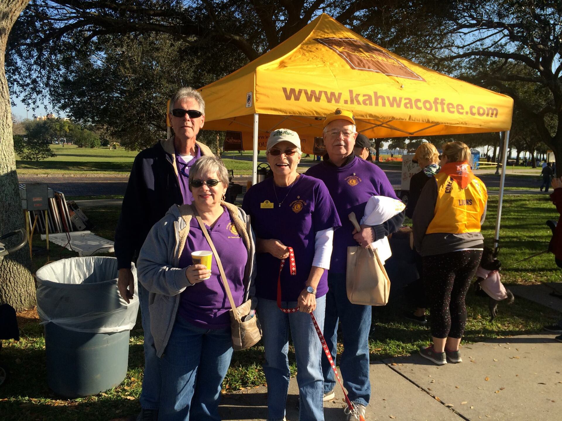 Four people wearing purple shirts stand near a yellow 
