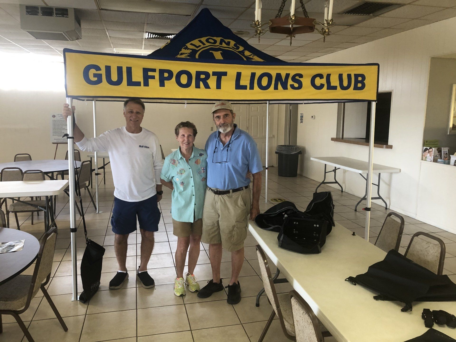 Three people under a Gulfport Lions Club canopy indoors.