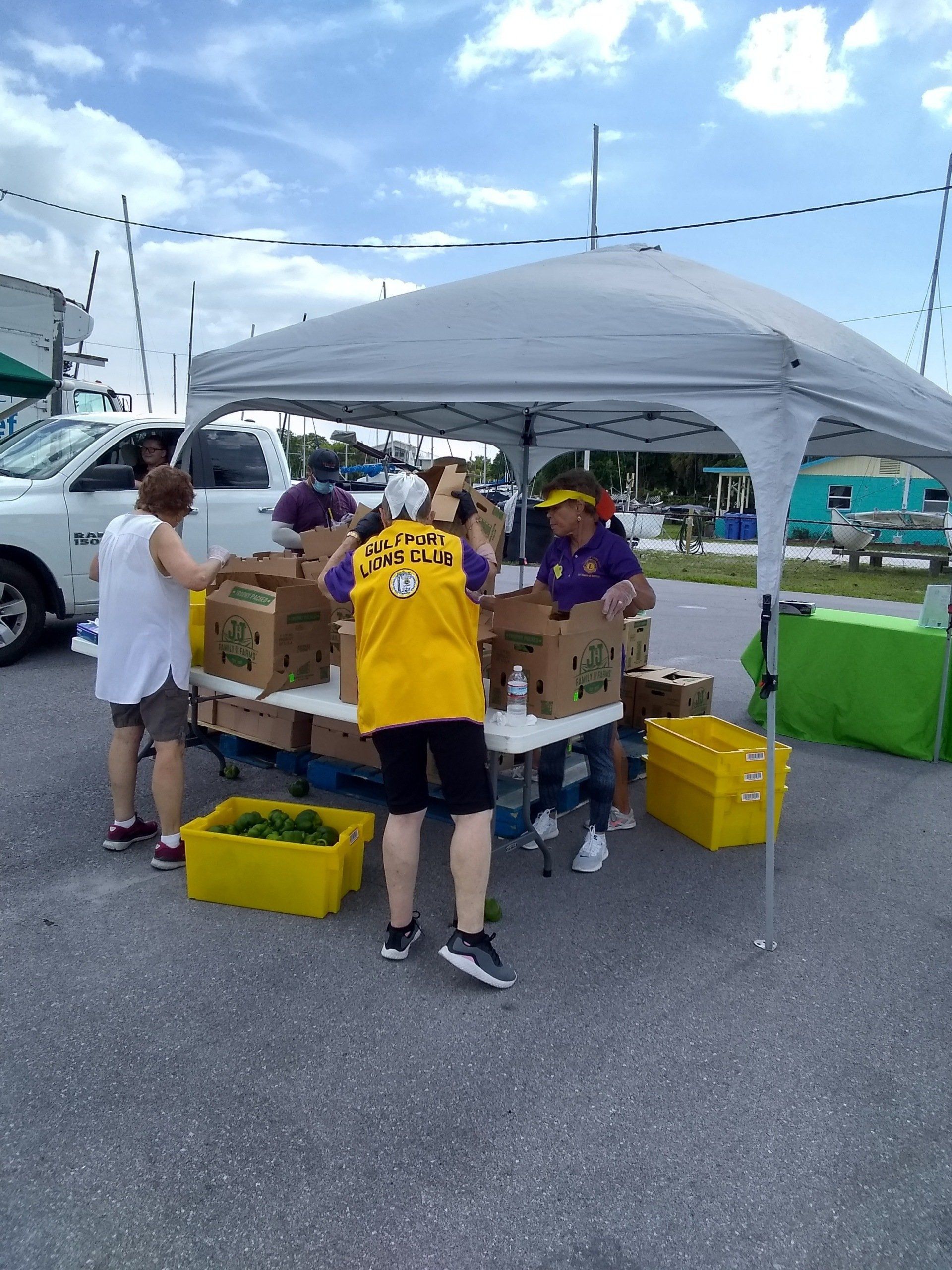 People at a farmer's market, under a canopy, sorting produce into boxes.