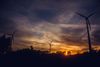 A group of wind turbines are silhouetted against a sunset sky.