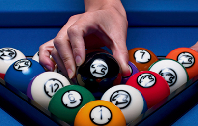 Pool table setup with cue stick, rack of numbered balls, and cue ball on a green felt surface.