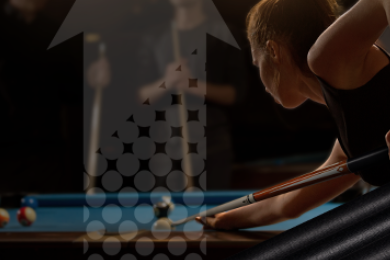 A person's hand holding a cue stick about to strike a white billiard ball on a green pool table, with a blue ball nearby.