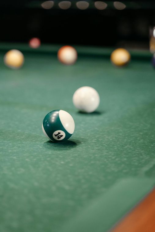 Pool table with a green felt surface and a green and white eight ball in focus. Other balls are scattered in the background.