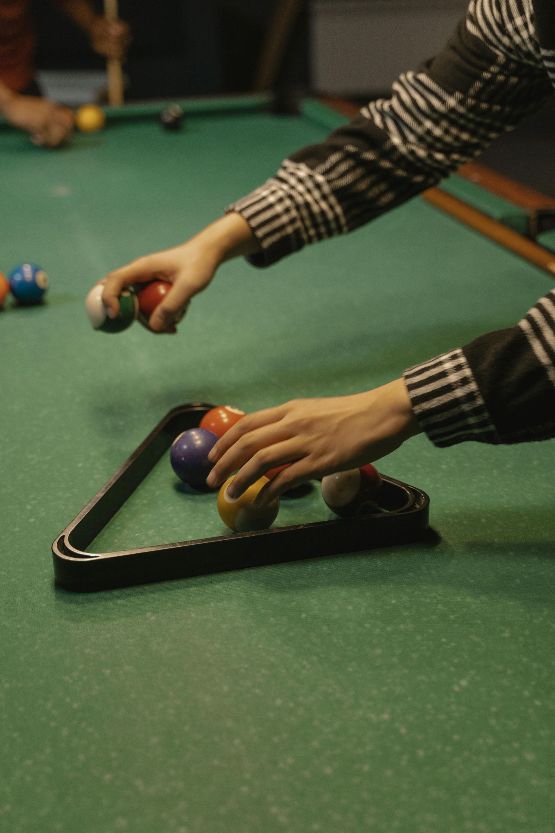 Person arranging billiard balls with a triangle rack on a green pool table, preparing for a game.