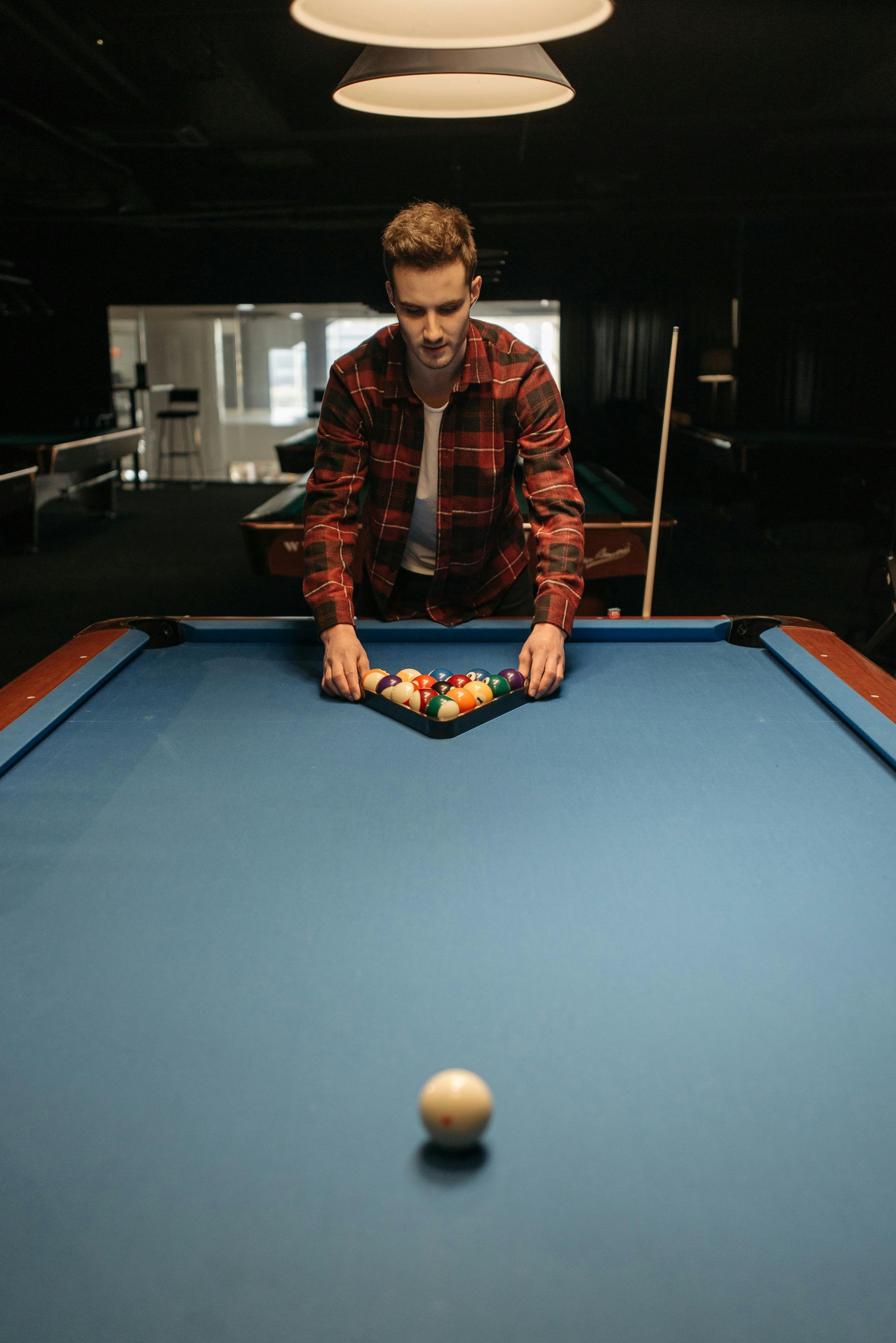 Man in plaid shirt setting up the pool balls in a triangle on a blue pool table.