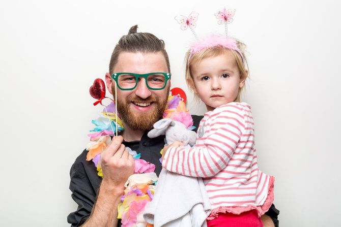 Man and young child holding colorful crafts, both wearing playful decorations against a white background