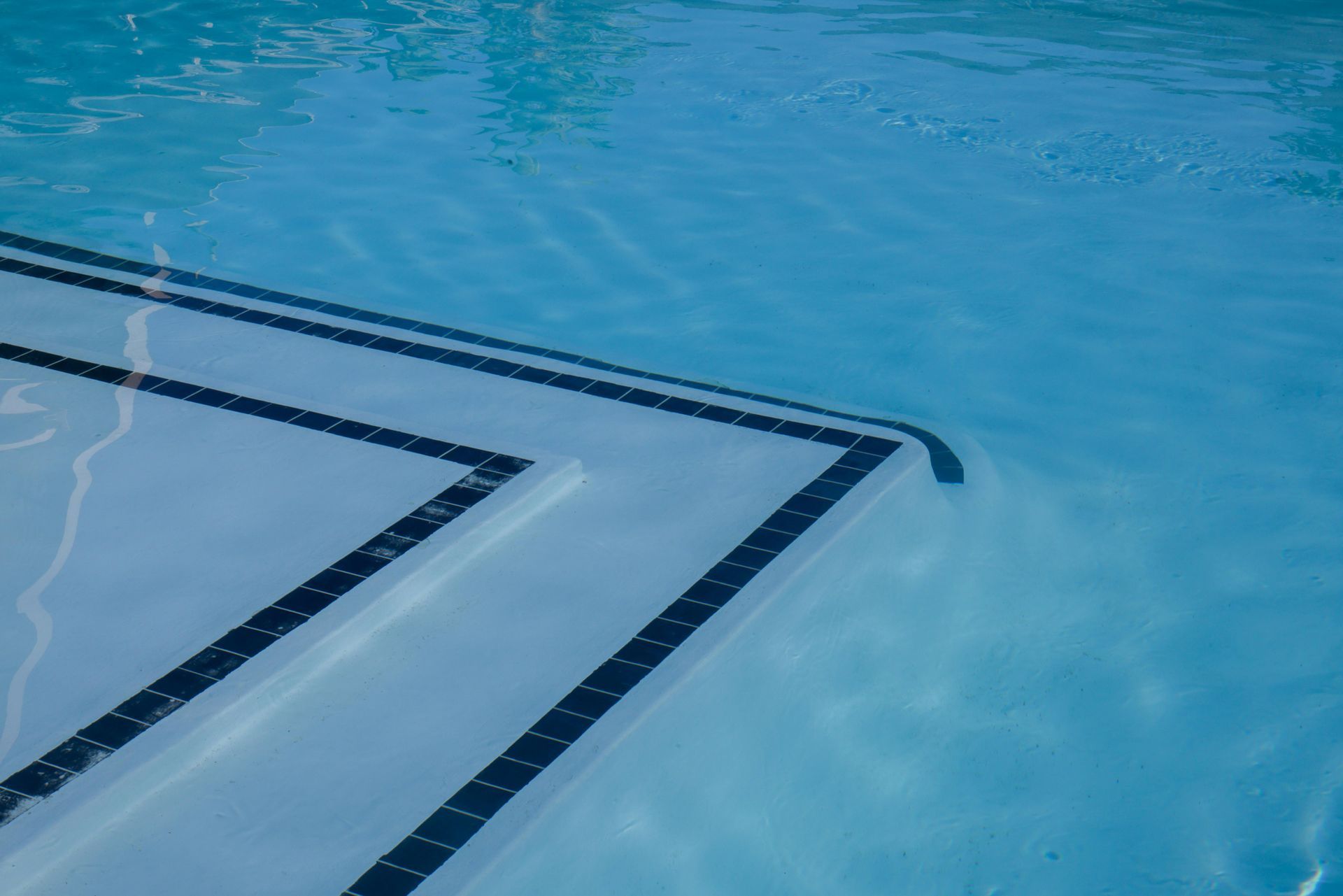The corner of a light blue swimming pool featuring dark tile accent lines along the steps and floor.